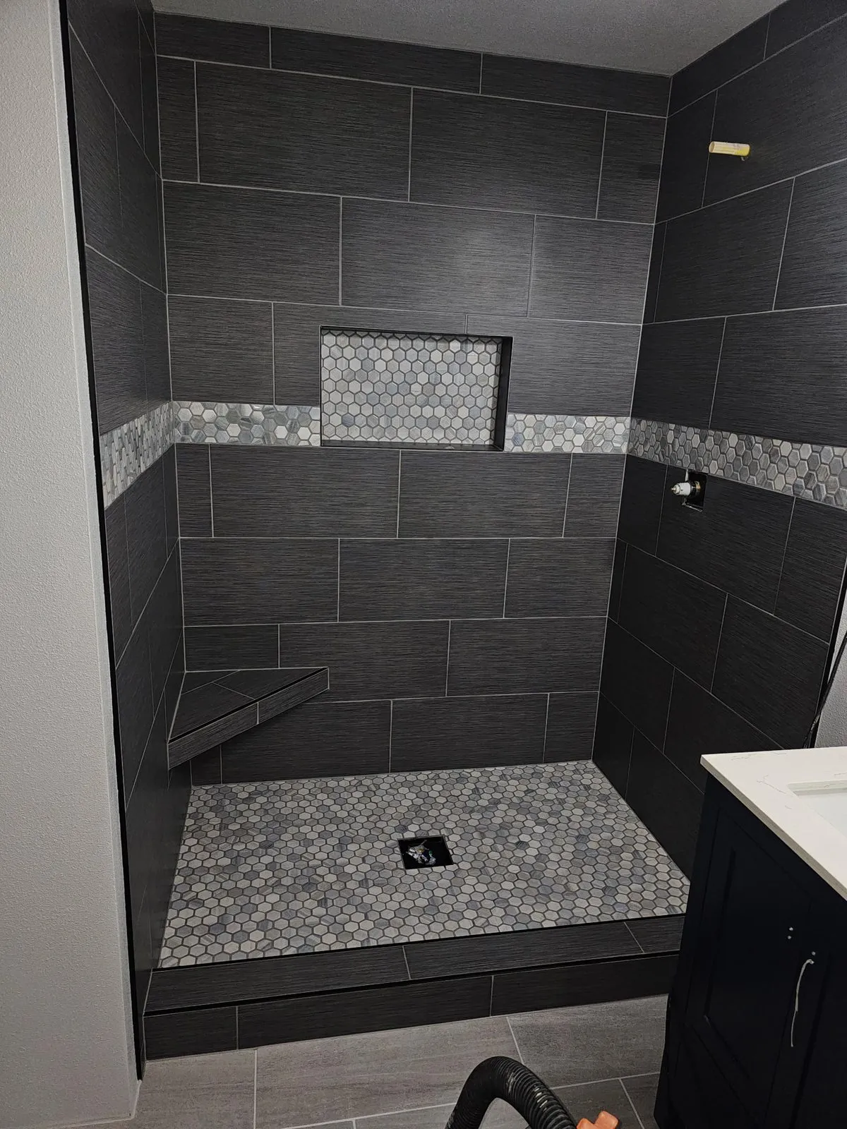 Charcoal tile shower with a mosaic accent band, niche and corner bench