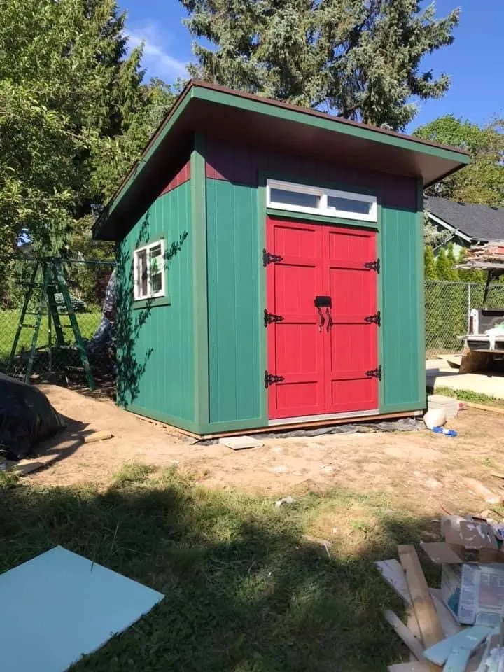 Finished green shed with red double doors and transom windows