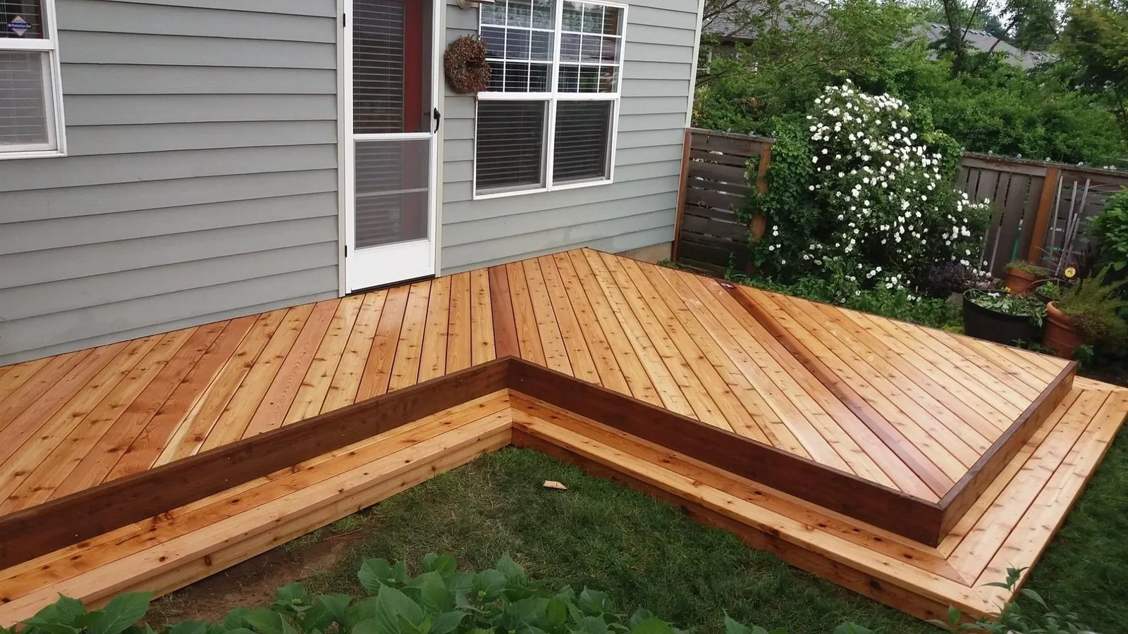 Finished L-shaped wood deck beside a gray house