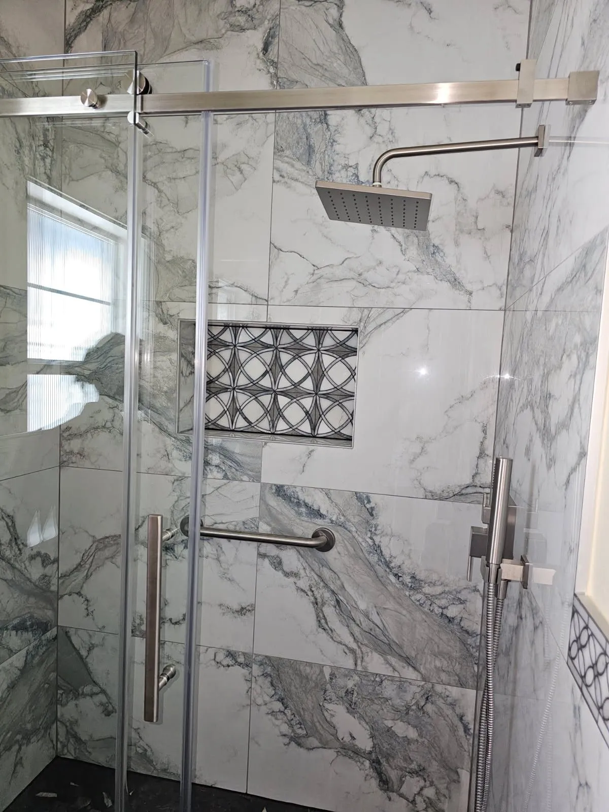 Marble-look shower with a sliding glass door, grab bar and mosaic niche