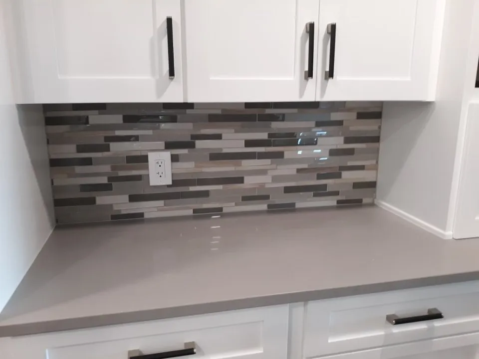 Gray linear mosaic backsplash between white cabinets and a quartz counter