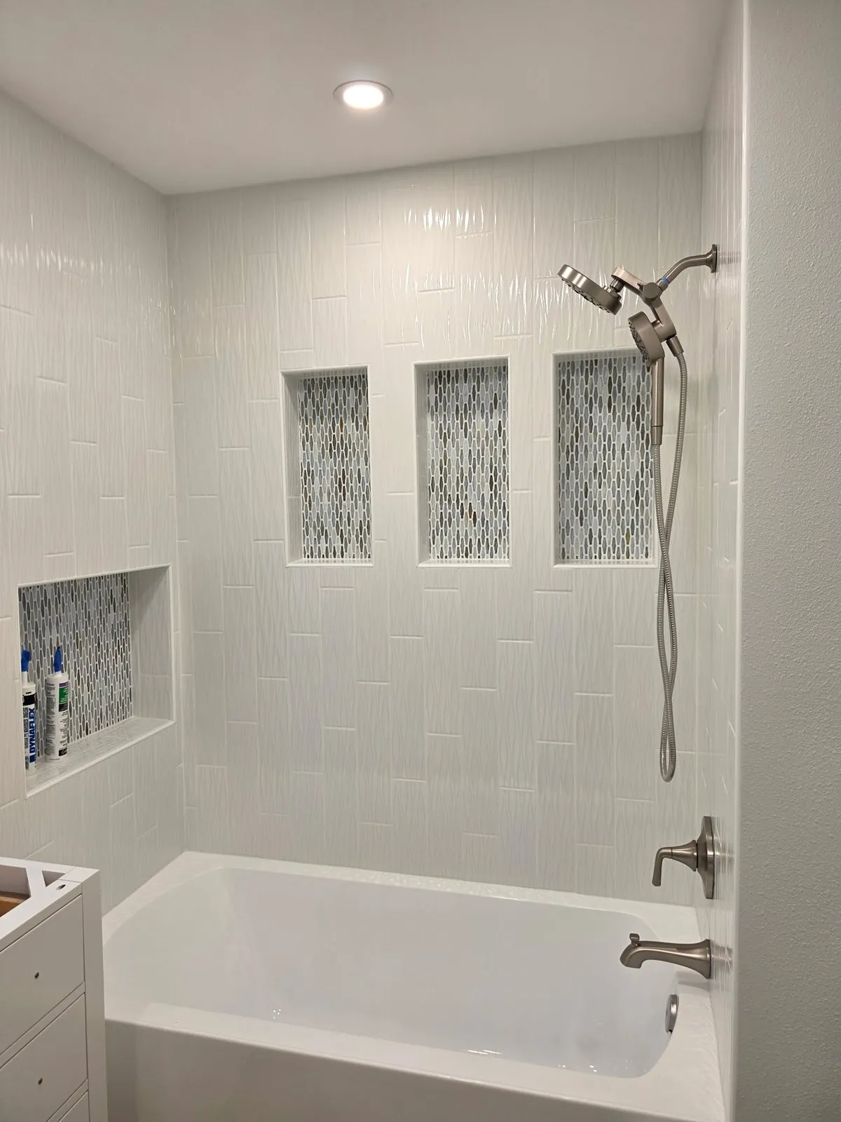 Tub surround with three mosaic-lined niches and a handheld shower