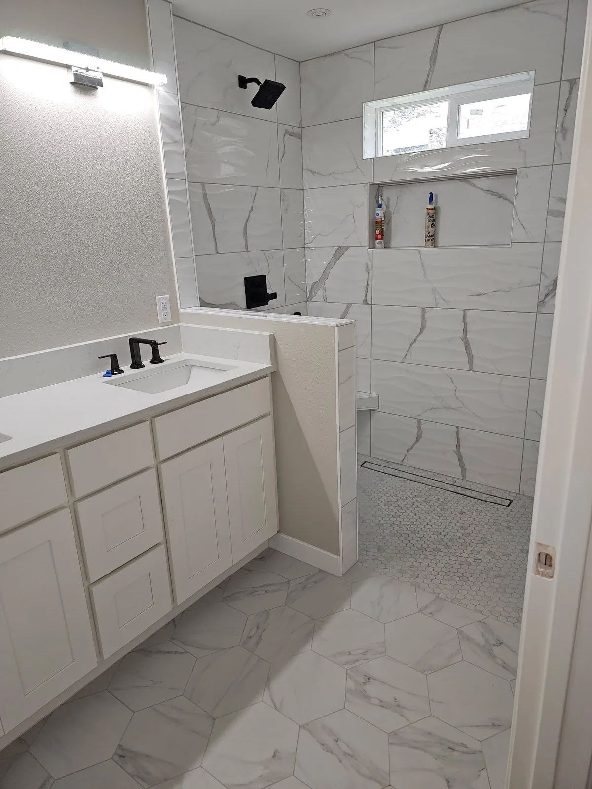 White vanity beside a marble-look walk-in shower with a window above the niche