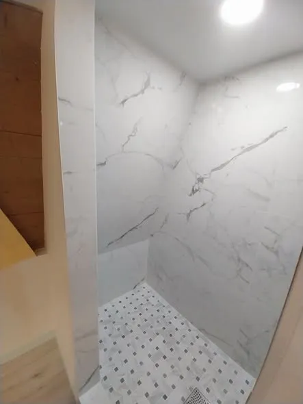 Corner view of the marble-look shower walls and mosaic floor