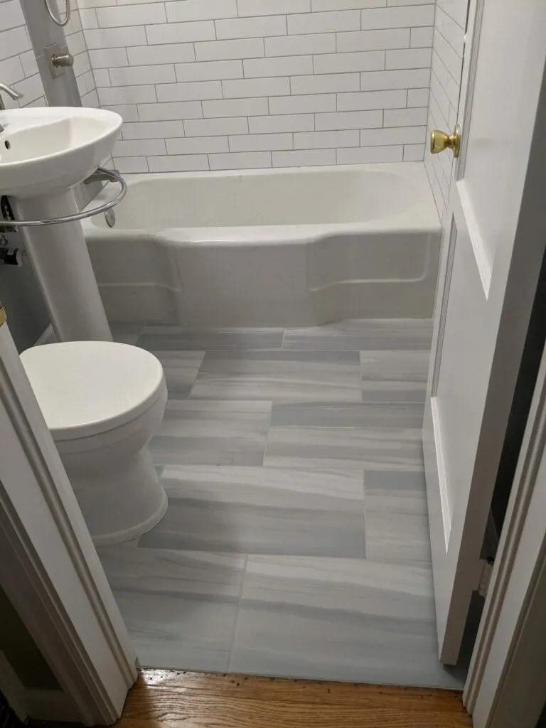 Tub bath with a pedestal sink on plank-look tile flooring
