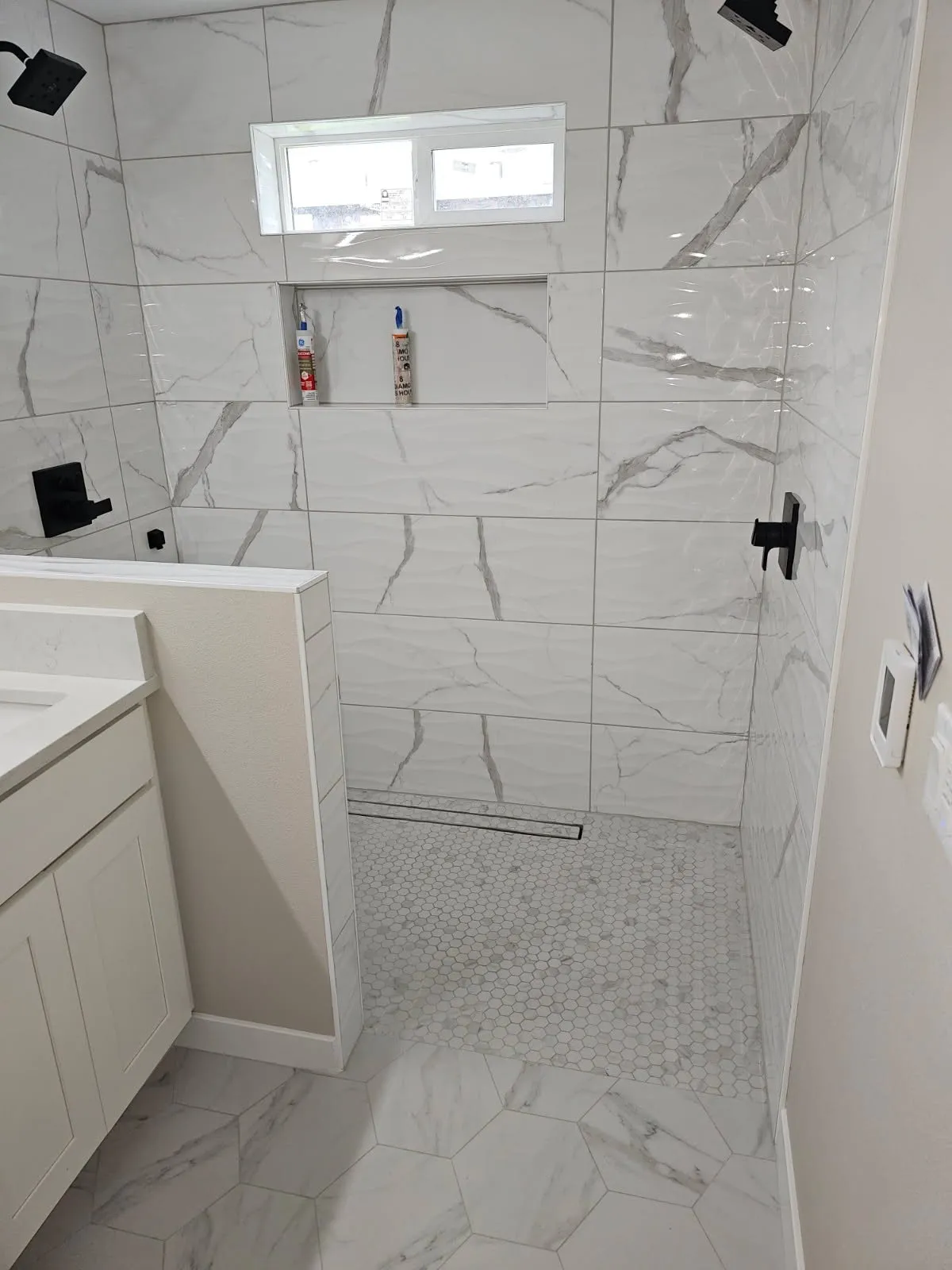 Walk-in shower with a half wall, linear drain and marble-look tile