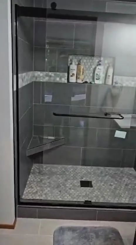 Charcoal tile shower with mosaic accent band and black glass slider
