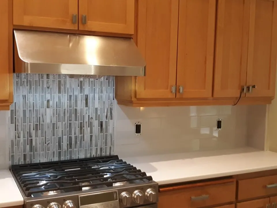 Vertical glass tile backsplash behind a gas range and hood